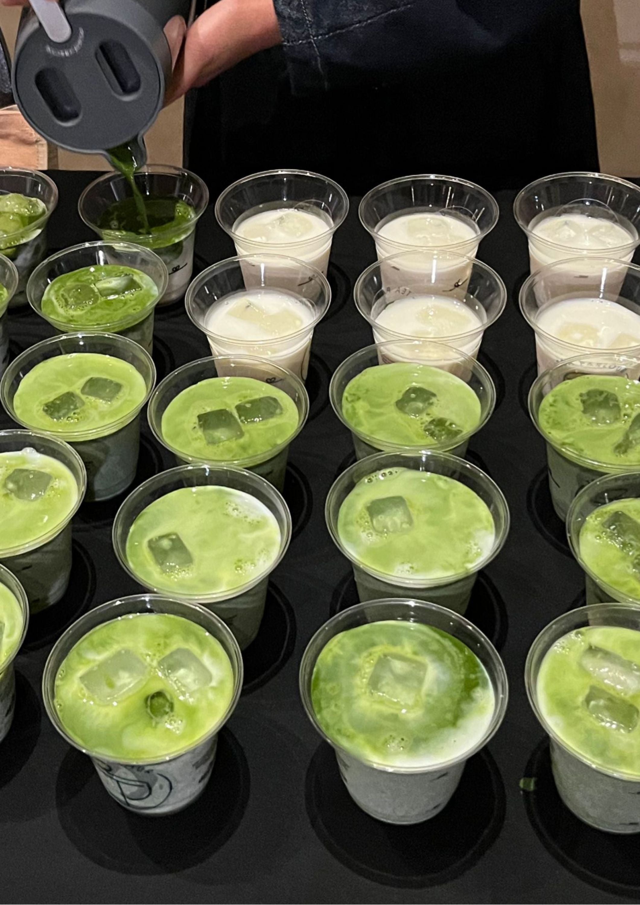 Matcha green tea being poured into iced cups during a Tea Parlour event on a black table setup.