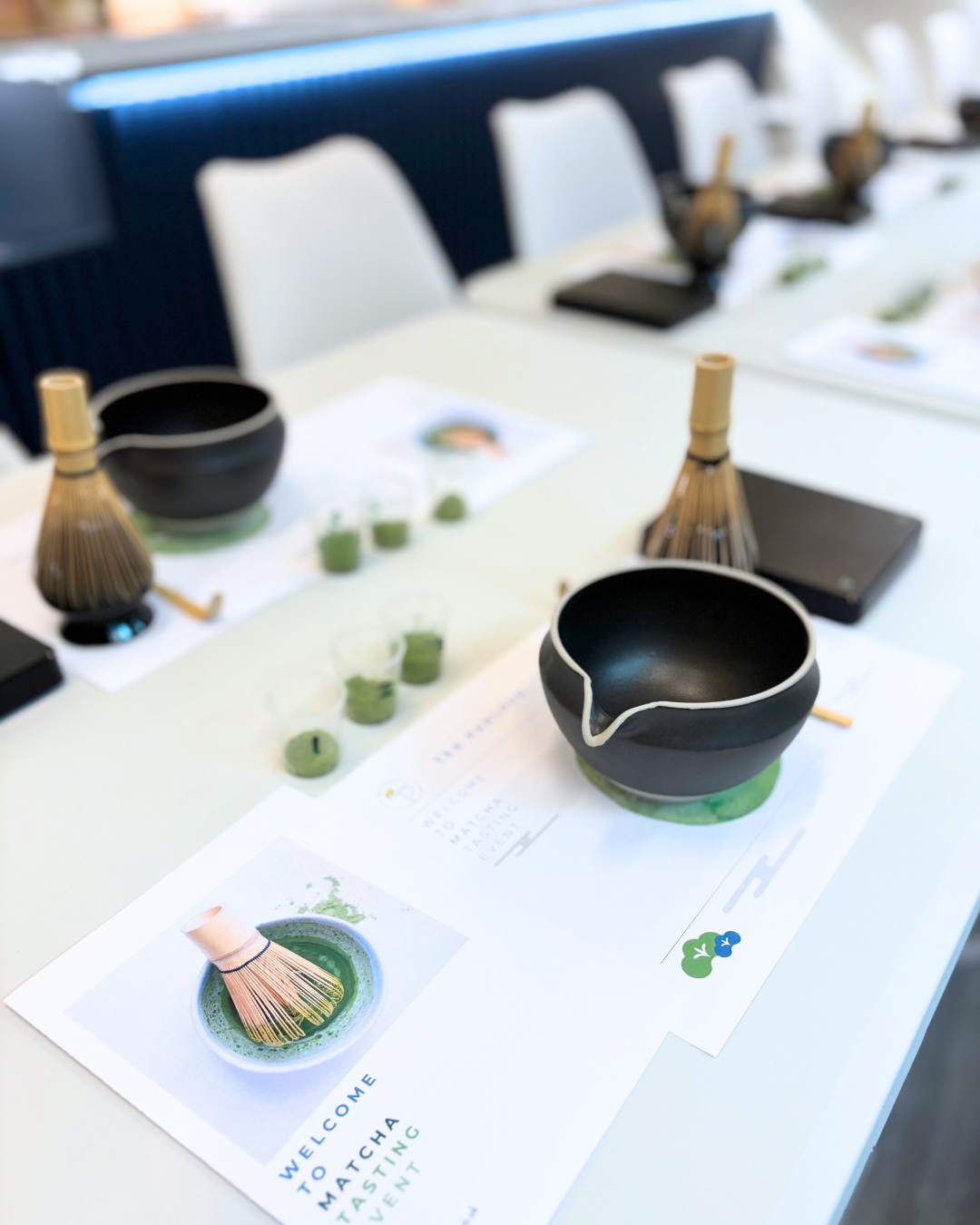 Tea-making setup with black tea bowl and whisk on a table with brochures.