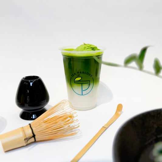 Premium Uji matcha latte topped with matcha ice cream, styled with bamboo whisk, chasen stand, and tea scoop on a white background at Tea Parlour.