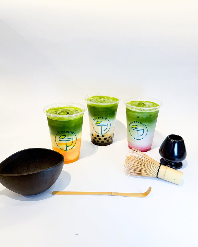 Three green drinks with boba in glasses on a white background, accompanied by a black bowl, wooden spoon, and black scoop.