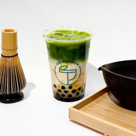 Bubble Uji matcha latte with black tapioca pearls in a clear cup, styled with a bamboo whisk and tea bowl on a wooden tray at Tea Parlour in London.