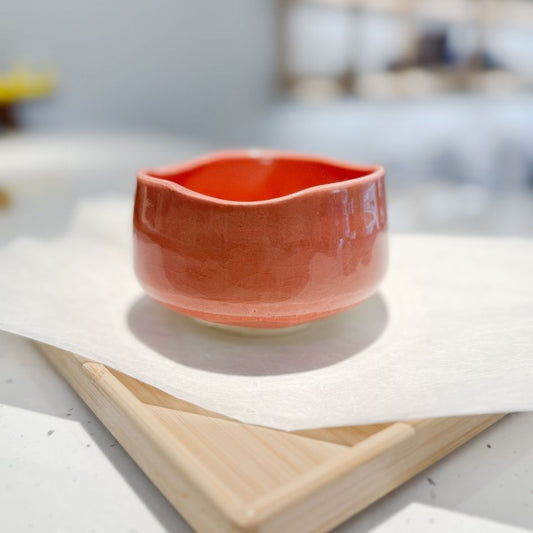 Red handcrafted ceramic matcha bowl (chawan) placed on a wooden tray with soft background at Tea Parlour in London.