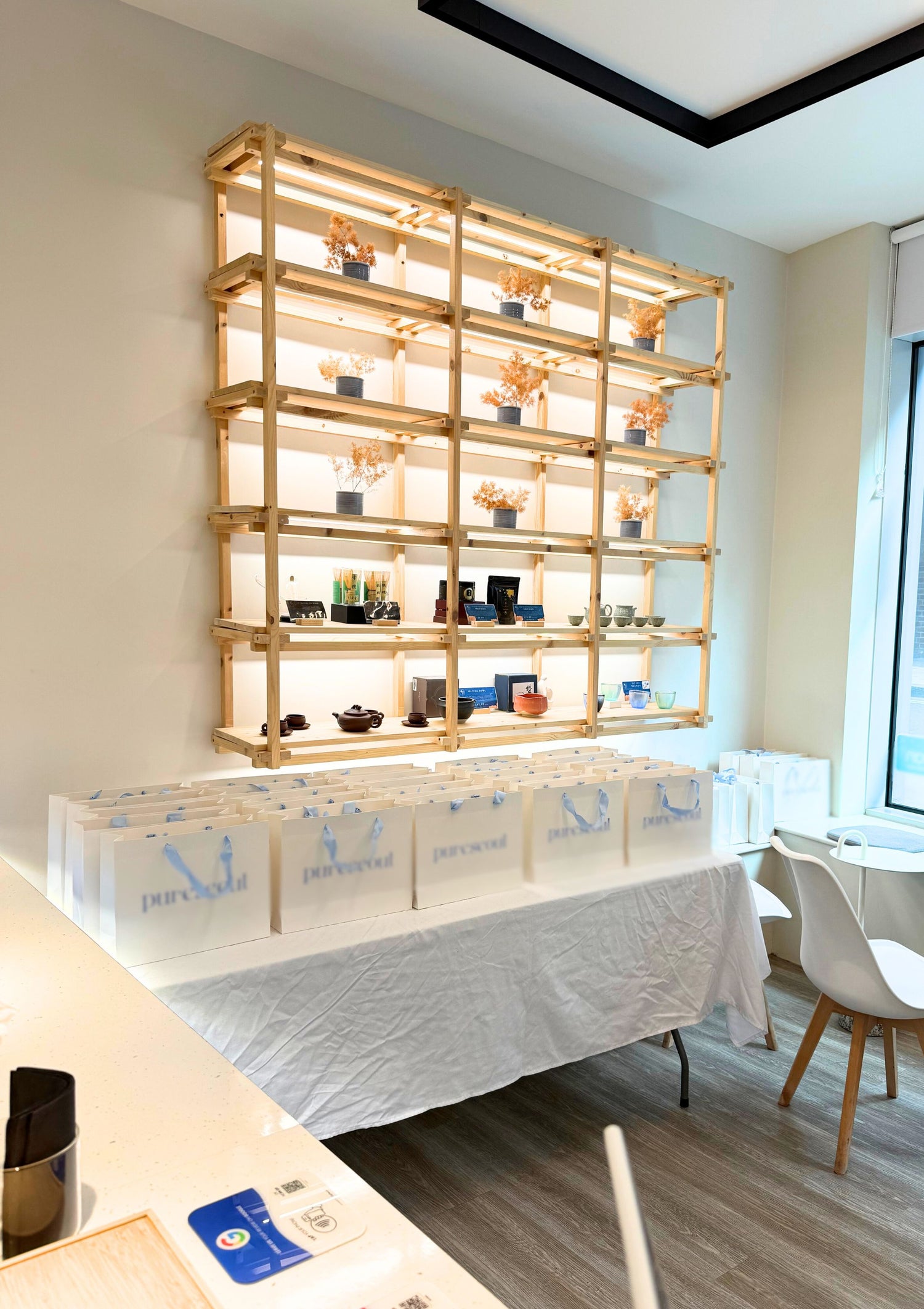 Tea Parlour event setup featuring wooden shelving with matcha tools, floral decor, and branded gift bags arranged on a table.