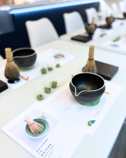 Tea-making setup with black tea bowl and whisk on a table with brochures.